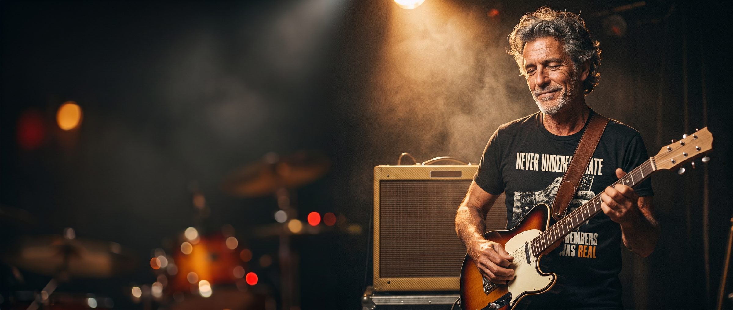 Grey-haired guitarist playing a sunburst electric guitar on a small bar stage, wearing the Rock Was Real tee